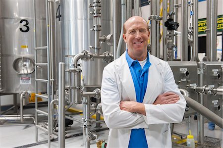 simsearch:6118-09129432,k - Caucasian male technician in a white coat standing near large stainless steel processing tanks in a bottling plant that makes flavoured water . Fotografie stock - Premium Royalty-Free, Codice: 6118-09129429
