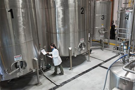 simsearch:6118-09129432,k - Caucasian female technician checking large stainless steel processing tanks in a bottling plant. that makes flavoured bottled water. Fotografie stock - Premium Royalty-Free, Codice: 6118-09129435