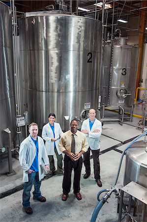 simsearch:693-06379749,k - Portrait of a team of Caucasian technicians and an African American management person standing next to large processing tanks in a bottling plant. Stock Photo - Premium Royalty-Free, Code: 6118-09129436