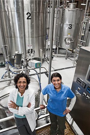 simsearch:6118-09129432,k - A portrait of a  multi-ethnic team of female technicians working near large processing tanks in a bottling plant. Fotografie stock - Premium Royalty-Free, Codice: 6118-09129438