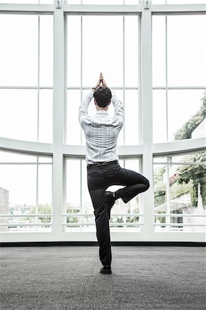 Businessman relaxing doing a yoga pose in a large open glass covered walkway. Stock Photo - Premium Royalty-Free, Code: 6118-09129590