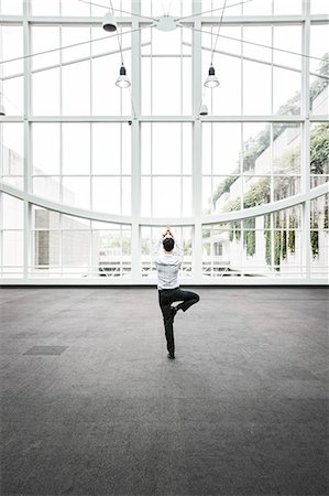 simsearch:6118-09129618,k - Businessman relaxing doing a yoga pose in a large open glass covered walkway. Photographie de stock - Premium Libres de Droits, Code: 6118-09129519