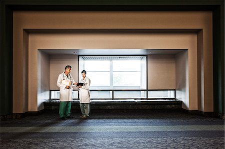 simsearch:6118-08842100,k - Caucasian man doctor and Asian woman doctor conferring in hospital hallway. Photographie de stock - Premium Libres de Droits, Code: 6118-09129675