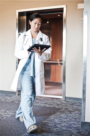 Asian woman doctor walking in a hospital hallway while working on a notebook computer. Stock Photo - Premium Royalty-Free, Code: 6118-09129696