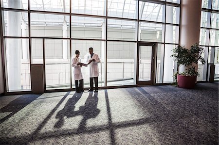 simsearch:6118-09129710,k - Man and woman doctors conferring over medical records in a hospital lobby. Stockbilder - Premium RF Lizenzfrei, Bildnummer: 6118-09129713