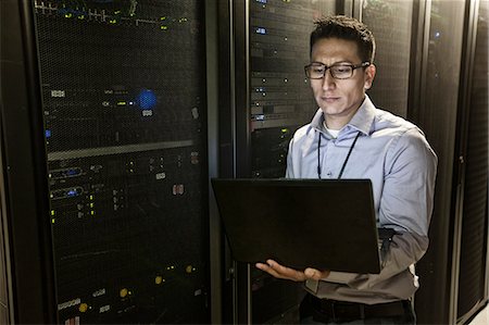Hispanic man technician doing diagnostic tests on computer servers in a large server farm. Stock Photo - Premium Royalty-Free, Code: 6118-09129836