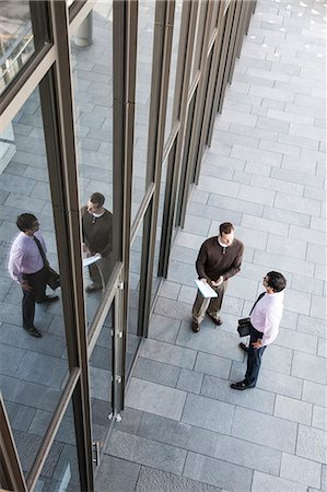 View from above of two businessmen meeting outside of a building next to a bank of windows. Stock Photo - Premium Royalty-Free, Code: 6118-09129974