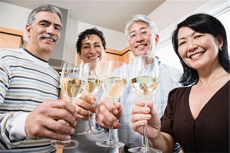 simsearch:614-06168767,k - Two couples in a kitchen, Asian and Caucasian men and women making a toast with glasses of white wine. Foto de stock - Sin royalties Premium, Código: 6118-09129996