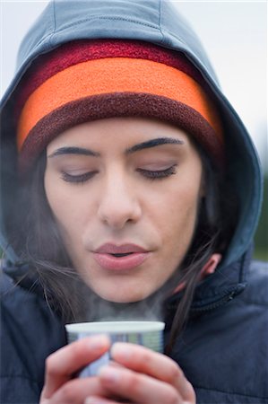 simsearch:649-02199405,k - Caucasian woman blowing on the surface of a hot cup of coffee on a winter day. Stockbilder - Premium RF Lizenzfrei, Bildnummer: 6118-09130013
