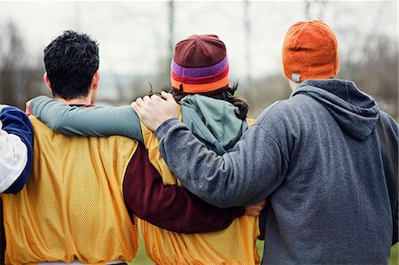 simsearch:832-03640620,k - View from behind of three friends with their arms around one another in sports kit and woolly hats. Foto de stock - Royalty Free Premium, Número: 6118-09130019