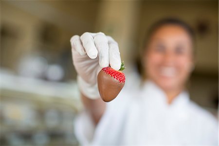 simsearch:6102-08942371,k - Hispanic woman holding a chocolate covered strawberry in a candy shop. Stock Photo - Premium Royalty-Free, Code: 6118-09130100