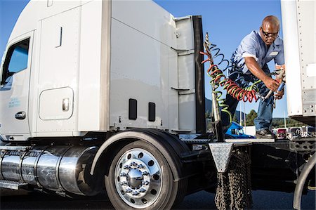 Black man truck driver attaching power cables from truck tractor to trailer at a truck stop. Stock Photo - Premium Royalty-Free, Code: 6118-09139365
