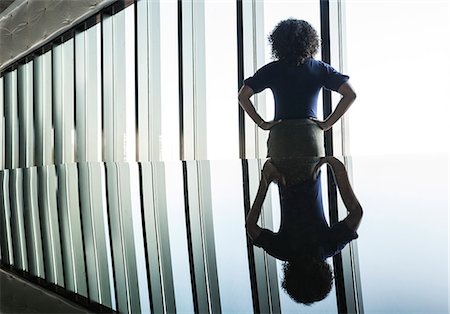 simsearch:6118-09139404,k - Black businesswoman reflected on the glass top of an office desk in front of a bank of windows. Photographie de stock - Premium Libres de Droits, Code: 6118-09139400