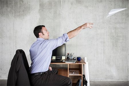 pov coffee cup - Caucasian businessman throwing a paper airplane while sitting at his desk in a raw office space. Stock Photo - Premium Royalty-Free, Code: 6118-09139409