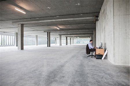 simsearch:614-08685284,k - Businessman sitting at a small desk in a large empty raw office space. Foto de stock - Sin royalties Premium, Código: 6118-09139410