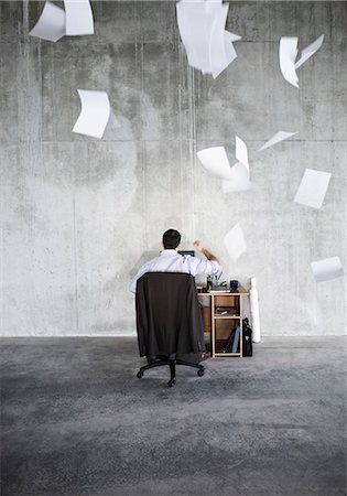 simsearch:6118-09139404,k - Caucasian businessman throwing papers in air while sitting at his desk in a large raw space. Photographie de stock - Premium Libres de Droits, Code: 6118-09139412