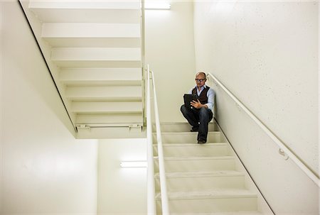 Asian businessman sitting in a stairwell working on a notebook computer. Stock Photo - Premium Royalty-Free, Code: 6118-09139434