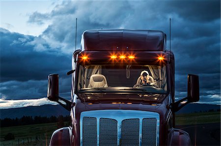 View into the cab of a  commercial truck with a driver in the front seat at night. Stock Photo - Premium Royalty-Free, Code: 6118-09139520