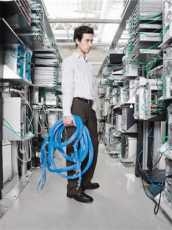 Male computer technician holding CAT 5 cables and standing in the aisle of a computer server farm. Stock Photo - Premium Royalty-Free, Code: 6118-09139628