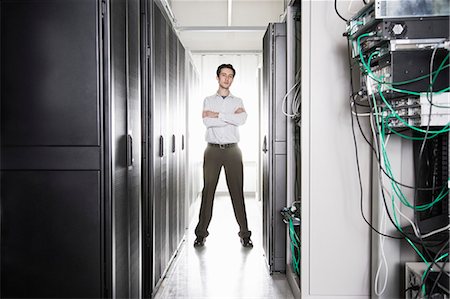 simsearch:6118-09139628,k - A male computer technician standing in an aisle of racks of servers in a computer server farm Foto de stock - Sin royalties Premium, Código: 6118-09139633