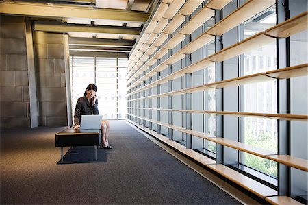 Caucasian businesswoman working on a laptop in the lobby of a large office building. Stock Photo - Premium Royalty-Free, Code: 6118-09139721