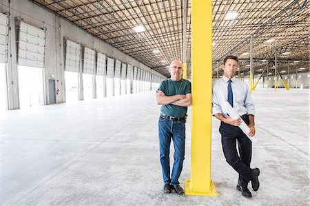 Two Caucasian men standing in front of loading dock doors in a new warehouse interior. Stock Photo - Premium Royalty-Free, Code: 6118-09139954