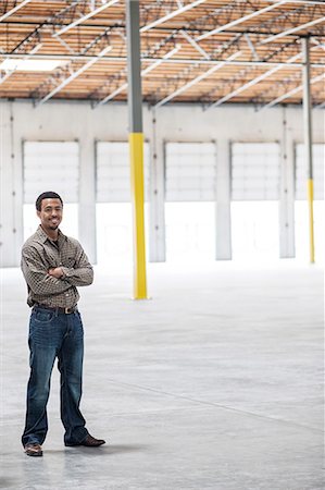 Black man owner of a new warehouse standing inside in front of loading dock doors. Stock Photo - Premium Royalty-Free, Code: 6118-09139923