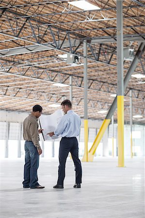 Back man owner of new warehouse and Caucasian man architect going over blue print plans of new interior layout. Stock Photo - Premium Royalty-Free, Code: 6118-09139924