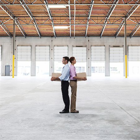 packages on loading dock - Caucasian man and black female holding cardboard boxes in middle of empty warehouse interior. Stock Photo - Premium Royalty-Free, Code: 6118-09139928