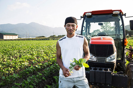 Japanese farmer standing in front of red tractor in a soy bean field, looking at camera. Stock Photo - Premium Royalty-Free, Code: 6118-09200144