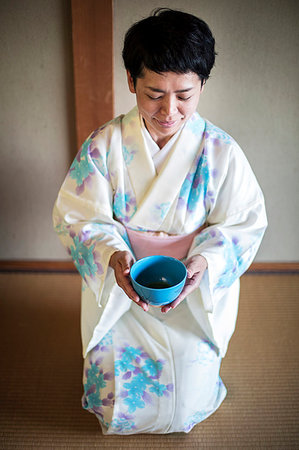 Japanese woman wearing traditional white kimono with blue floral pattern kneeling on floor during tea ceremony, holding blue tea bowl. Stock Photo - Premium Royalty-Free, Code: 6118-09200247