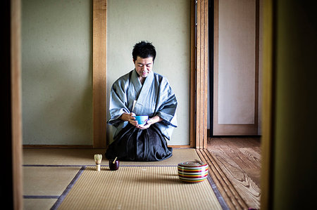 simsearch:6118-09200284,k - Japanese man wearing traditional kimono kneeling on tatami mat, holding tea bowl, during tea ceremony. Stock Photo - Premium Royalty-Free, Code: 6118-09200251