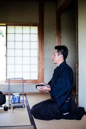 simsearch:6118-09200260,k - Japanese man wearing traditional kimono kneeling on floor, holding tea bowl, during tea ceremony. Photographie de stock - Premium Libres de Droits, Code: 6118-09200256
