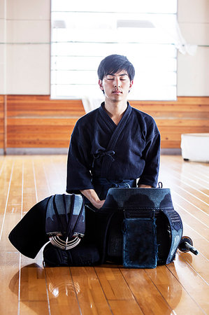 Female Japanese Kendo fighter kneeling on wooden floor, fastening