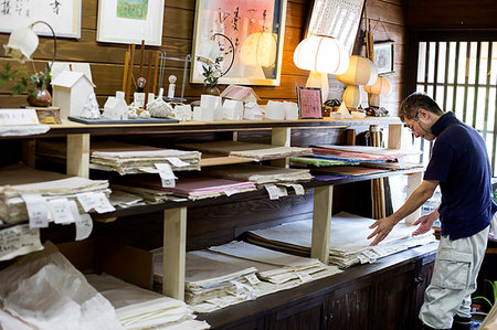 simsearch:6118-09200557,k - Japanese man in a traditional workshop with a display of handcrafted washi papers and small objects. Fotografie stock - Premium Royalty-Free, Codice: 6118-09200419