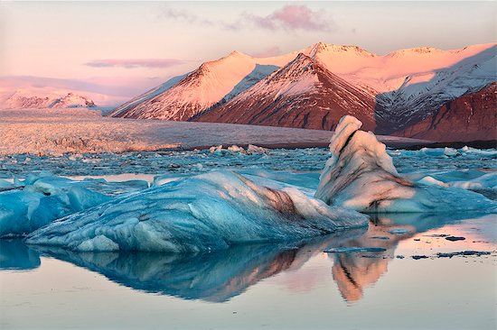 View across the calm water of Jokulsarlon glacial lagoon towards snow-capped mountains and icebergs bathed in winter morning light, at the head of the Breidamerkurjokull Glacier on the edge of the Vatnajokull National Park, South Iceland, Iceland, Polar Regions Stock Photo - Premium Royalty-Free, Image code: 6119-07781110