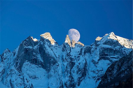 The moon appears behind the snowy mountains illuminating the peaks at sunset, Bondasca Valley, Swiss Alps, Switzerland, Europe Foto de stock - Sin royalties Premium, Código: 6119-08420413