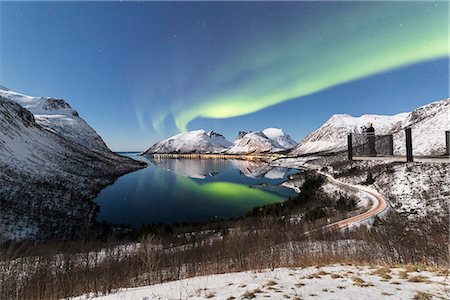 Photographer on platform admires the Northern lights (aurora borealis) and stars reflected in the cold sea, Bergsbotn, Senja, Troms, Norway, Scandinavia, Europe Foto de stock - Sin royalties Premium, Código: 6119-09074129