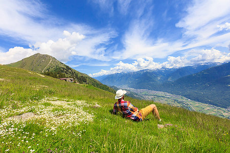 simsearch:6119-09127077,k - Man with hat relaxes on green meadows looking towards Morbegno, Alpe Bassetta, Valtellina, Sondrio, Lombardy, Italy, Europe Stock Photo - Premium Royalty-Free, Code: 6119-09203023