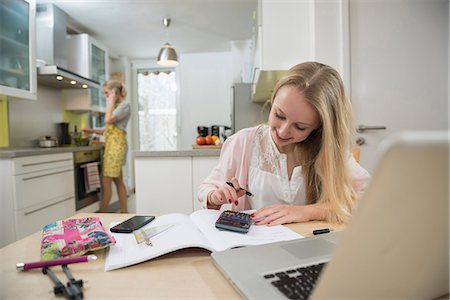 Teenage girl doing homework while her mother preparing lunch, smiling Photographie de stock - Premium Libres de Droits, Code: 6121-07740236