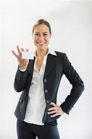plain background - Portrait of businesswoman in black suit holding blank business card, smiling Stock Photo - Premium Royalty-Free, Code: 6121-07741362