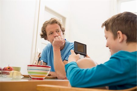 pyjamas (sleepwear with pants) - Father looking at son playing video game at breakfast table Stock Photo - Premium Royalty-Free, Code: 6121-07809657