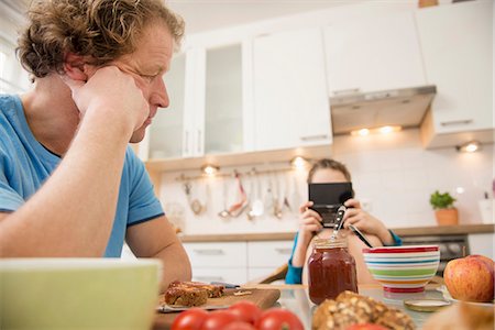 pyjamas (sleepwear with pants) - Father looking at son playing video game at breakfast table Stock Photo - Premium Royalty-Free, Code: 6121-07809656