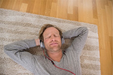 Relaxed man lying on rug listening to music Stock Photo - Premium Royalty-Free, Code: 6121-07809687