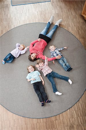 Female educator and four kids relaxing on ground in kindergarten, elevated view Photographie de stock - Premium Libres de Droits, Code: 6121-07810107