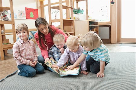 Female educator and four kids sitting on  ground of kindergarten looking at picture book Photographie de stock - Premium Libres de Droits, Code: 6121-07810106