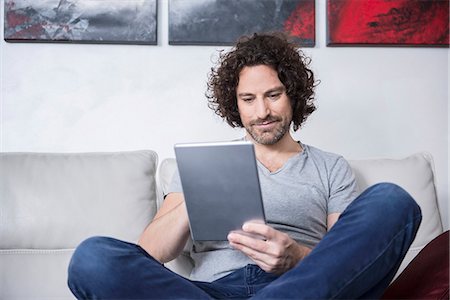 Man sitting on couch and using a digital tablet, Munich, Bavaria, Germany Foto de stock - Sin royalties Premium, Código: 6121-07992589