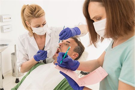 Female dentist examining patient and dictating the findings to the assistant, Munich, Bavaria, Germany Photographie de stock - Premium Libres de Droits, Code: 6121-08228454