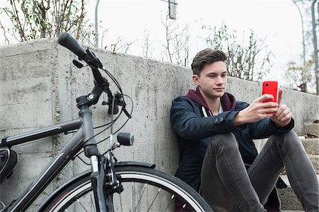 Young man text messaging on mobile phone and leaning against wall, Munich, Bavaria, Germany Foto de stock - Sin royalties Premium, Código: 6121-08522151