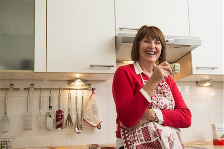 Happy senior woman wearing apron and drinking espresso coffee in kitchen, Munich, Bavaria, Germany Photographie de stock - Premium Libres de Droits, Code: 6121-08522191